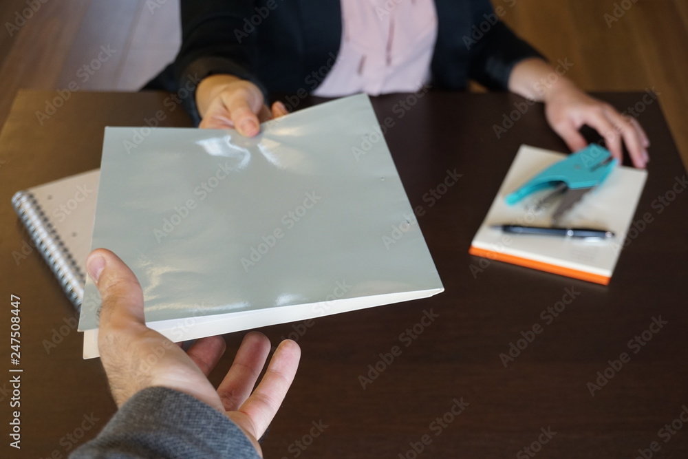 Woman is handing over a white file in direction camera while sitting at ...