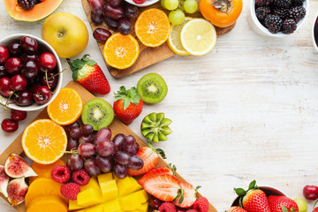 Wall Mural - Healthy raw fruits background, cut mango, strawberries raspberries oranges plums apples kiwis grapes blueberries cherries, on white table, copy space, top view, selective focus