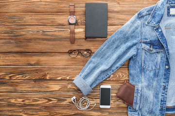 Flat lay with denim jacket, smartphone and accessories on wooden background