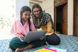 © IndiaPix - Happy village girl sitting with her mother on a cot at home operating a laptop computer.