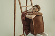 © LIGHTFIELD STUDIOS - beautiful young woman holding vintage leather bag and sitting near ladder isolated on beige