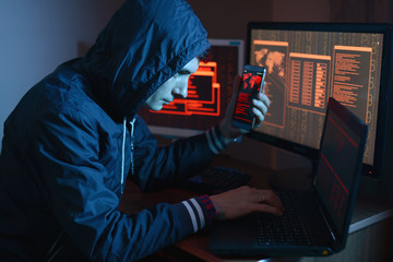 Hacker in the hood holding the phone in his hands trying to hack the mobile device cloud. The concept of cyber security