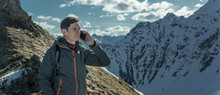 Man Speaking On The Phone On The Top Of A Snowy Mountain Far From Civilization. Activity And Communication Availability