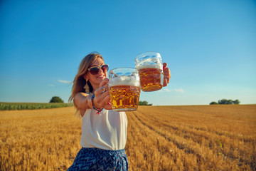 Happy girl holding beer glass in a big wheat-field.