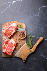 Wall Mural - Raw Fresh Marbled Meat Beef Steak rosemary, spices  and vintage ax  on a wooden board. Black marble background. Top View Copy space for Text