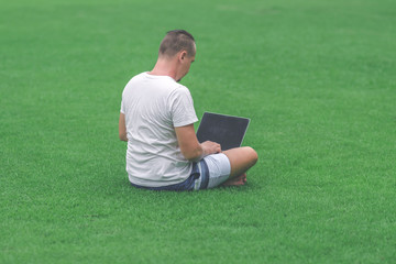 Young man in the green tropical park working online with laptop. Freelancer man on Bali island concept.