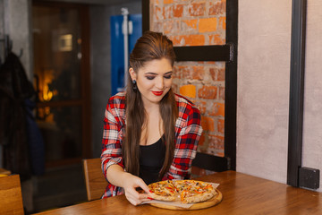 Beautiful and sexy girl sitting by the window in a cafe and eating pizza.