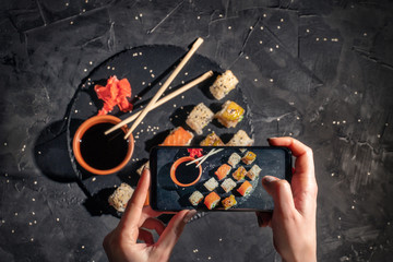 Wall Mural - Hands taking photo a different assortment of sushi rolls with smartphone