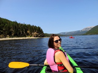 A young female tourist in a kayak exploring the beautiful waters in Bonne Bay with a group of kakayers, in Gros Morne National Park, Newfoundland, Canada.  She is looking back smiling and happy. 