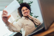 © Mediteraneo - Smiling young African female entrepreneur sitting at a desk in her home office make selfie photo.