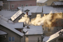 Smoking Chimneys At Roofs With Snow Of Houses Emits Smoke, Smog At Sunrise, Pollutants Enter Atmosphere. Environmental Disaster. Harmful Emissions, Exhaust Gases Into Air. Winter Day, Heating Season.