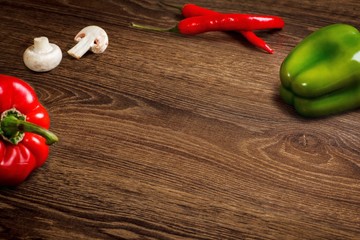 Dark wooden table surface. Decorated by mushrooms, sweet red pepper, red and green pepperoni. Clean center.