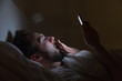 Adult sleepy yawning man awake late at night in bed surfing in web/ sleepy tired, social media addiction, dependency on a cell phone, half-closed tired eyes, negative effect on the eyes, sleeplessness