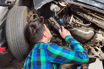 Handsome car mechanic checking suspension system of a lifted car at repair service station .