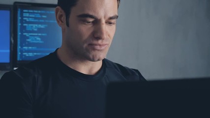 Portrait of developer programmer working on computer in a data center filled with monitor screens. Steadicam shot