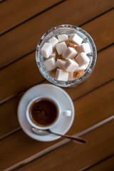 A small white porcelain espresso cup on a saucer with a teaspoon and two pieces of sugar