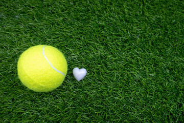 Wall Mural - Tennis ball with white heart shape on green grass