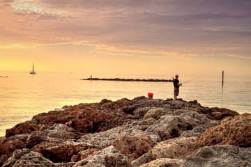 Wall Mural - Fisherman on the rocks of South Marco Island Beach at Sunset with a boat in the distance