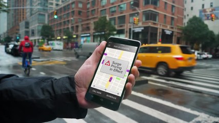 A man uses a ride-sharing app on his cellular phone to call a driver and notices a surge pricing pop-up warning.	Shot at 60fps.  	