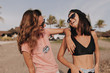 © PhotoBook - Two women friends in stopt outfit walking and have fun on the beach near the ocean on bakcground of palm trees in sunlight