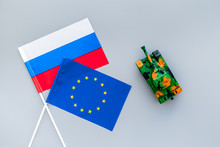 War, Confrontation Concept. European Union, Russia. Tanks Toy Near European And Russian Flag On Grey Background Top View
