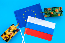 War, Confrontation Concept. European Union, Russia. Tanks Toy Near European And Russian Flag On Blue Background Top View