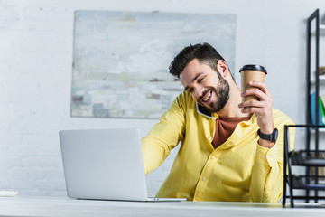 Wall Mural - Cheerful bearded businessman talking on smartphone and holding paper cup