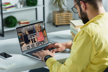 bearded man looking at laptop with online booking website on screen in modern office