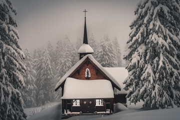 A beautiful small wooden chapel standing in the frozen winter forest in the Mythen Region, Switzerland