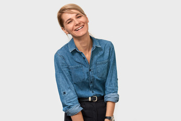 Horizontal studio portrait of happy blonde European woman smiling broadly standing in blue denim shirt over white background. Business female posing on studio wall with copy space for your promotion