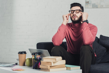 Wall Mural - bearded man in glasses sitting near laptop on sofa