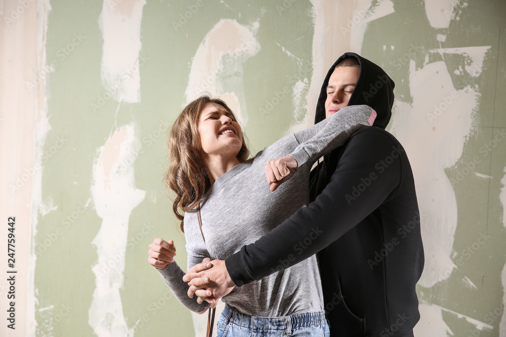 Young woman defending herself from attack by thief on color background