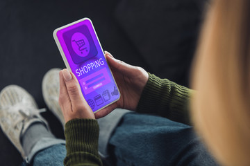 cropped view of woman holding smartphone with shopping app on screen