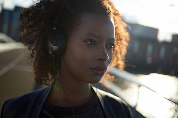 Wall Mural - Beautiful black woman wearing headphones in urban city setting during sunrise