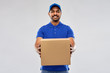 © Syda Productions - mail service and shipment concept - happy indian delivery man with parcel box in blue uniform over grey background