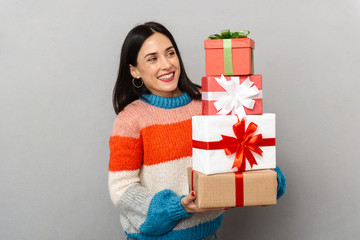 Photo of surprised woman 30s holding bunch of gift boxes while standing, isolated over gray background