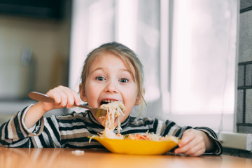 Wall Mural - girl eating pasta with sausage in the kitchen in a striped jacket