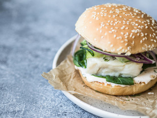 Homemade fish burger of white fish fillet with cucumber slice, red onion, fresh dill and spinach on a white plate