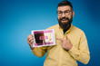 © LIGHTFIELD STUDIOS - Happy bearded man pointing at digital tablet with online tickets app, isolated on blue