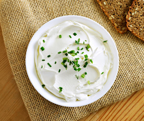 Cream cheese, quark or yogurt in a white bowl. Dairy product with fresh herbs, healthy eating theme. wooden table background.