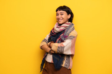 Wall Mural - Young hippie woman over yellow wall keeping the arms crossed while smiling