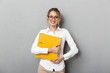 Photo of happy businesswoman wearing glasses holding paper folders in the office, isolated over gray background