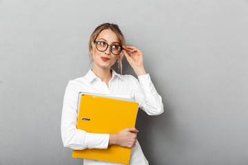 Canvas Print - Photo of successful secretary wearing glasses holding paper folders in the office, isolated over gray background