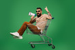 © LIGHTFIELD STUDIOS - bearded man with megaphone pointing up while sitting in shopping cart isolated on green