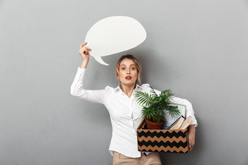 Canvas Print - Portrait of excited woman holding box with office belongings and blank bubble for text, isolated over gray background