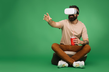 Wall Mural - bearded man with soda using Virtual reality headset isolated on green