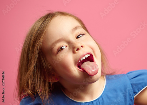 Fotomural Close up shot of little girl with her tongue out over pink isolated