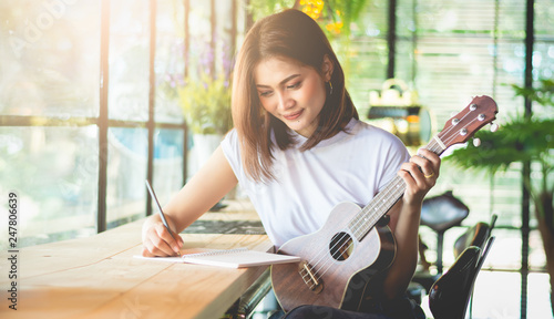 Fotografía Female composer is writing music in a joyful feeling using ukulele as a device in the Vintage-style Café, Soft tone vintage style