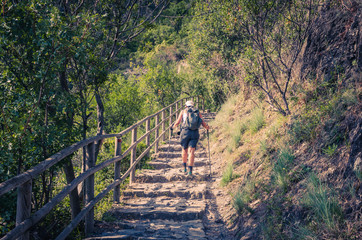 tourist woman is hiking up steps of pedestrian stone path trail stairs with railing between cornigli