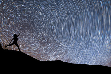 Wall Mural - beautiful starry night, female silhouette jumping on the star trails background. night landscape.